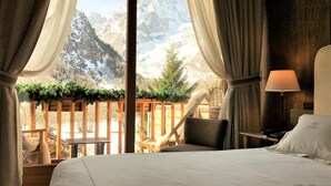 A bedroom with a bed, a chair, a nightstand, and a lamp. There is a view of mountains through the window. - Auberge de La Maison (Courmayeur)