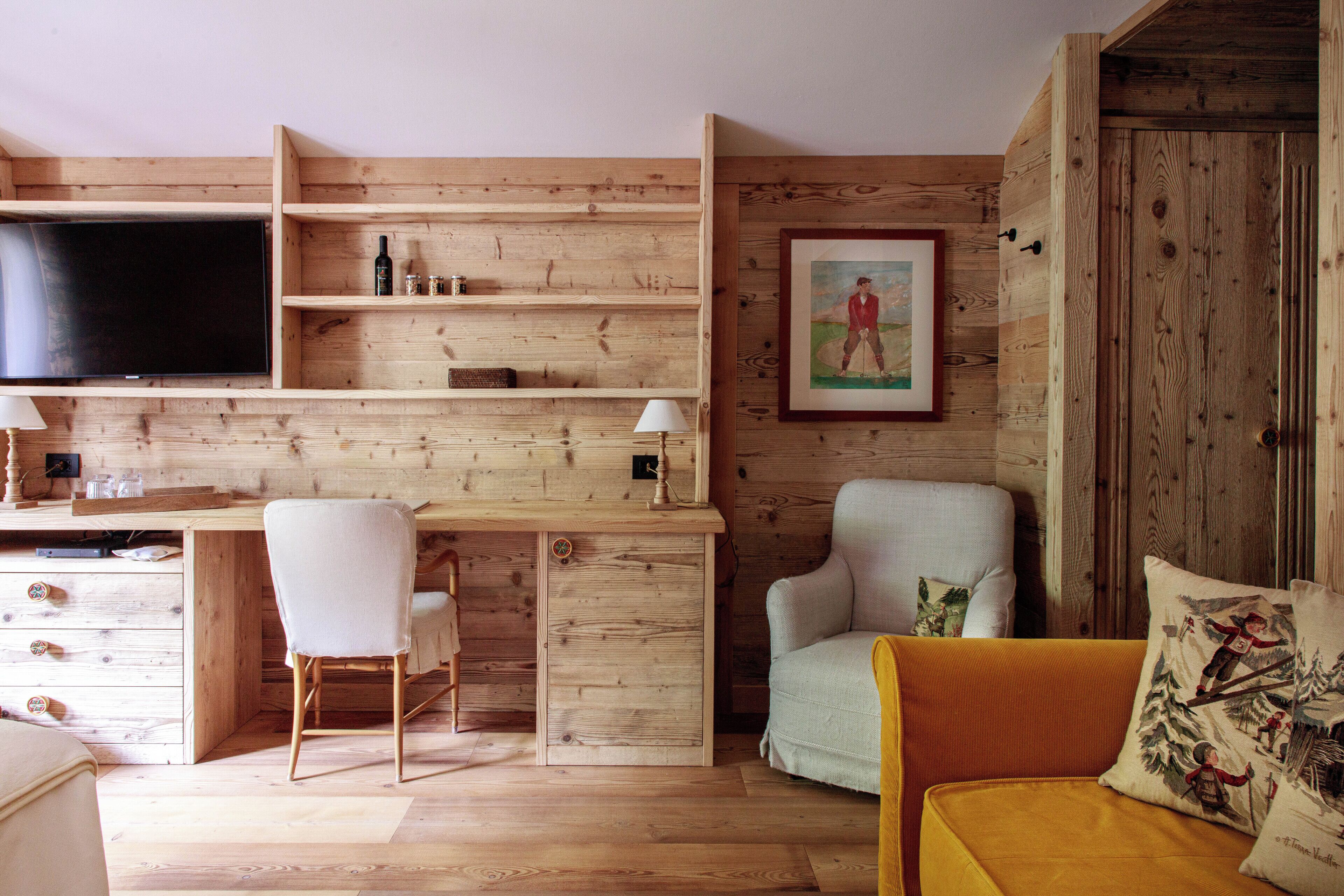 A wooden interior with a desk, two chairs, a sofa, and a television.