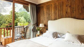 A bedroom with a large bed, a wooden headboard, a nightstand with a lamp, and a view of a balcony with a chair and a vase of flowers.