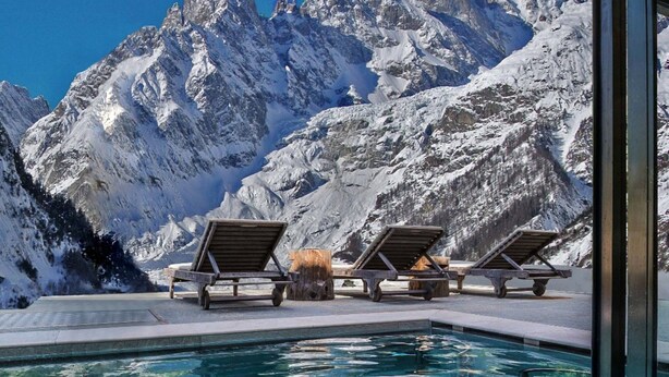 A pool with clear blue water, surrounded by lounge chairs and a mountain backdrop. - Auberge de La Maison (Courmayeur)