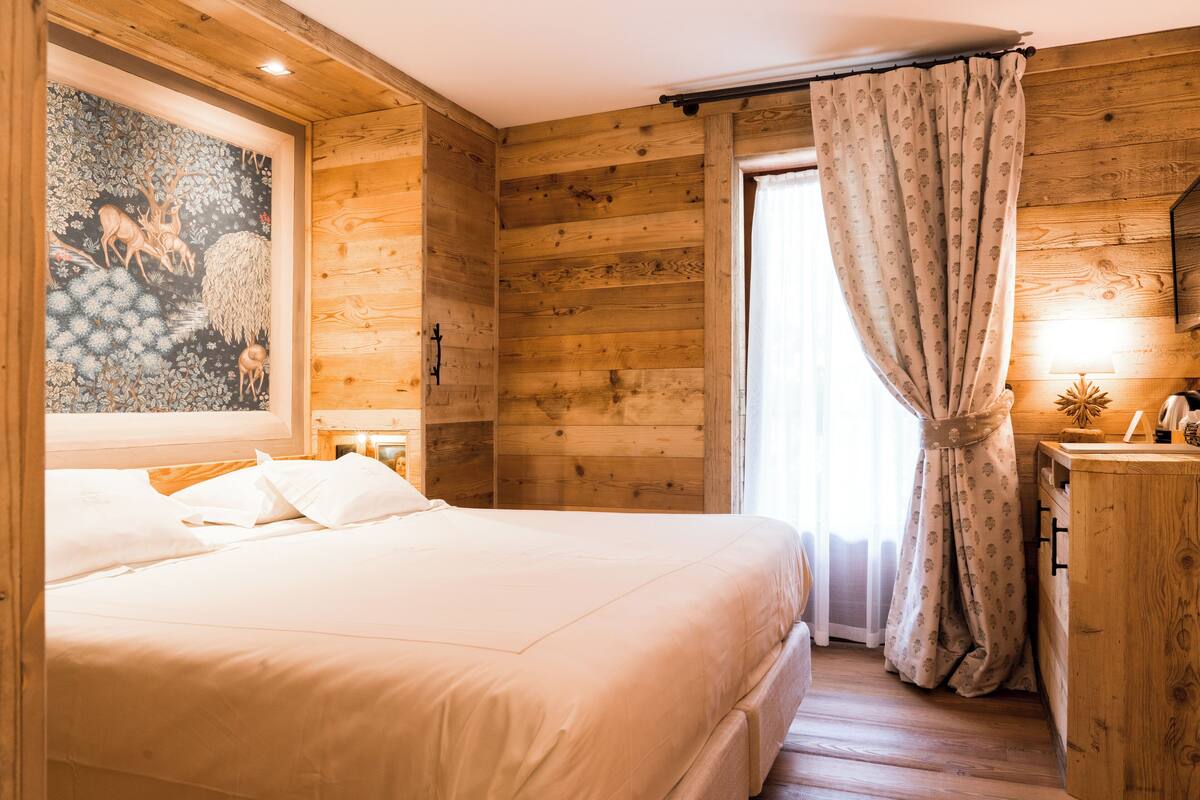 Una habitación de madera con una cama, un cuadro, una ventana con cortinas y un aparador de madera.