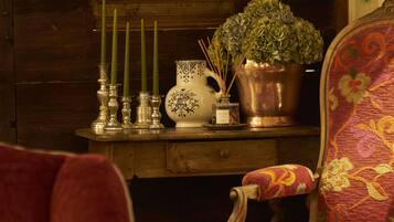 Een knus interieur met een houten wand, een decoratieve krans, een vaas met groene planten en een stoel met bloemenstof.