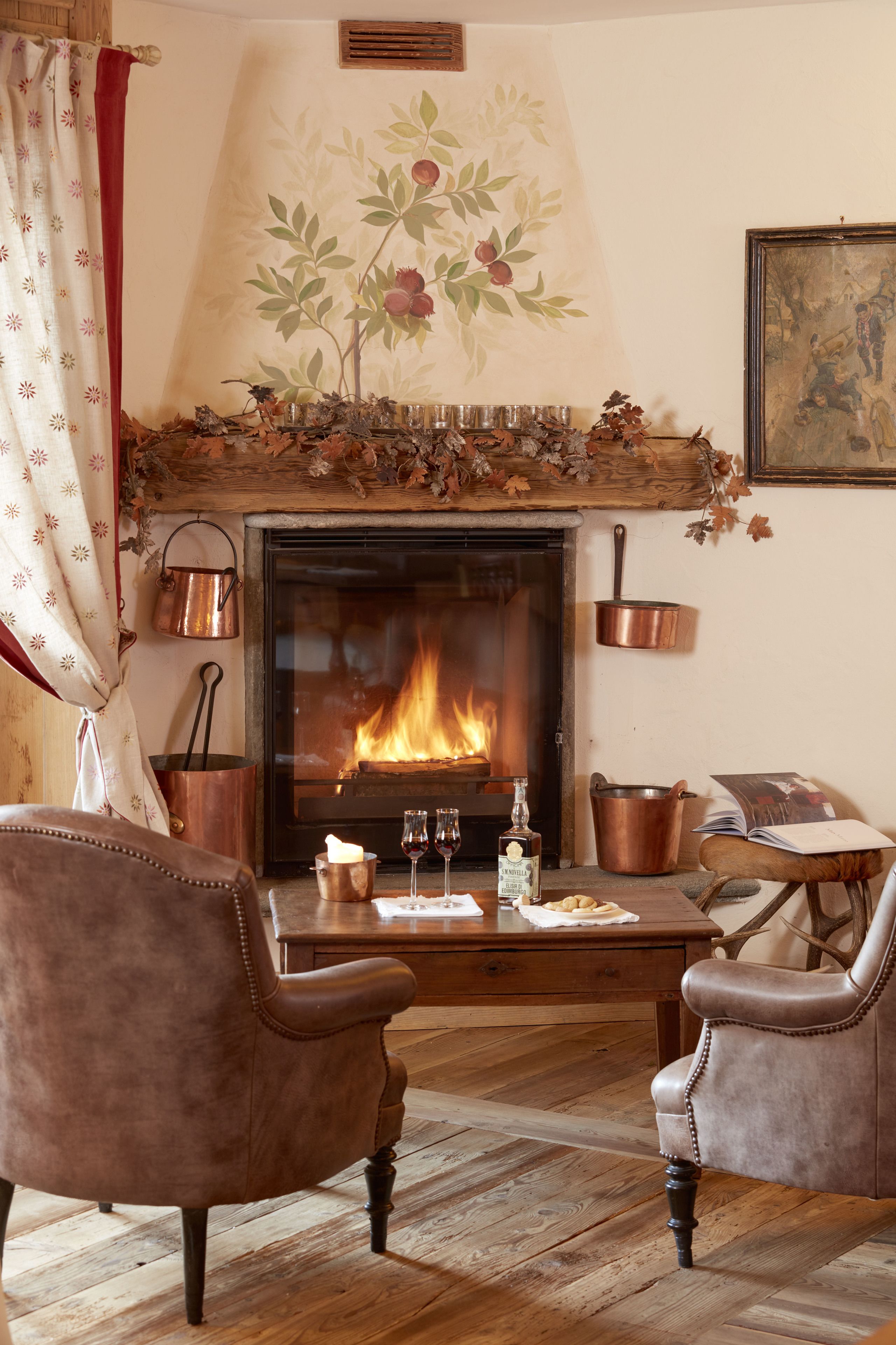 Una sala de estar acogedora con chimenea, sillones de cuero, una mesa de centro con un libro y vasos, y un mural decorativo.