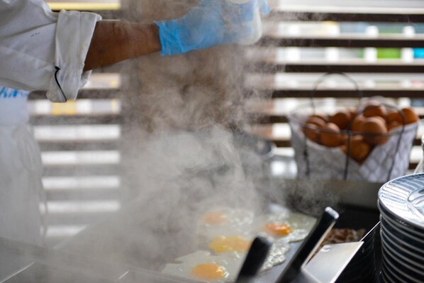 A person cooking eggs on a hot griddle, steam rising from the pan.
