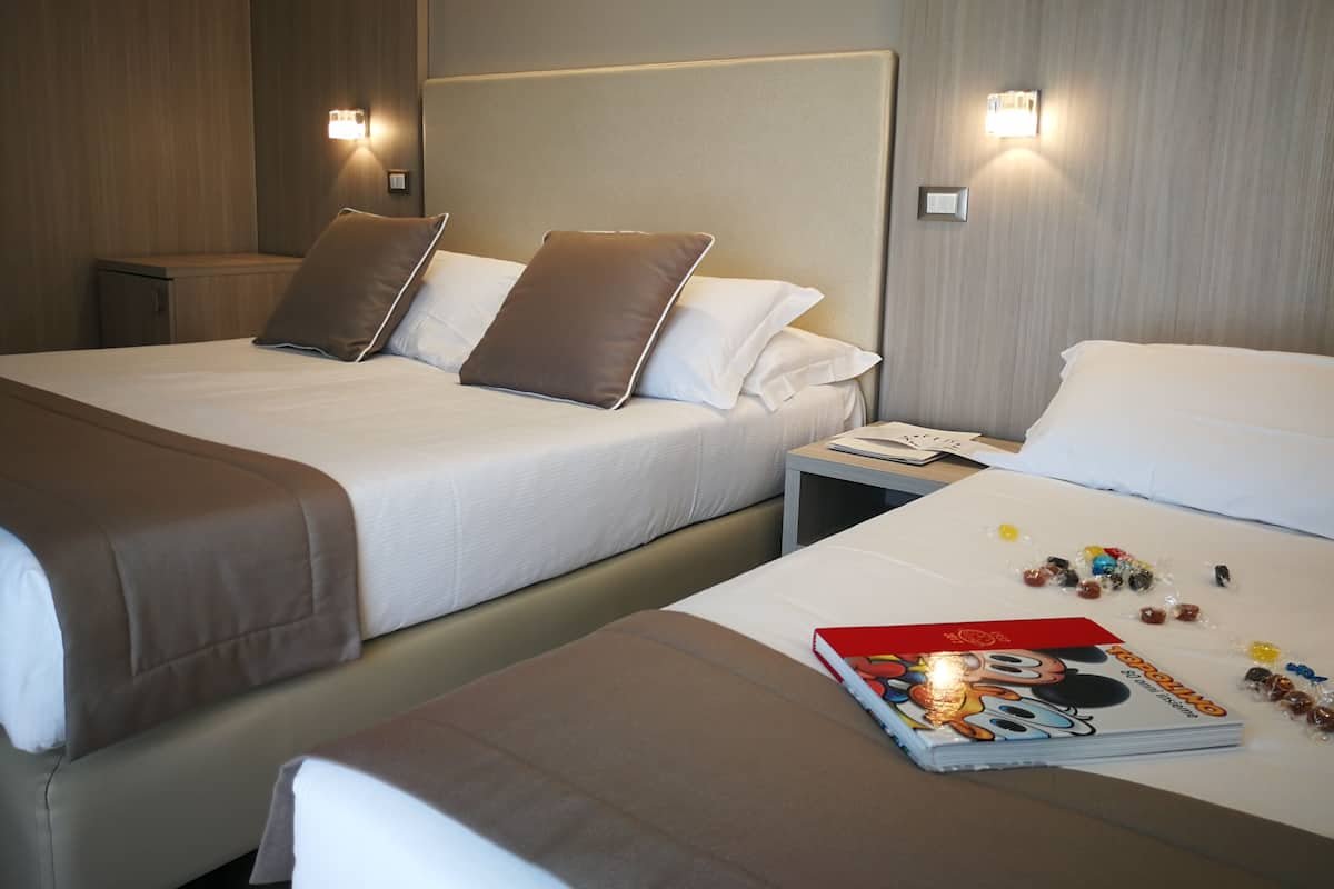 A hotel room with two beds, each with a headboard and bedside tables. There are pillows on the beds and a magazine on the right bed.