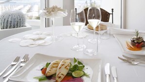 A dining table set with white tableware, a plate of food, and wine glasses, with a view of the ocean through large windows. - Hotel delle Nazioni (Jesolo)