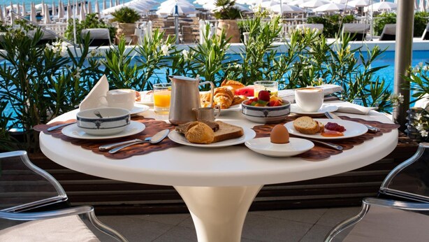 A breakfast table with various food items and a view of the pool and beach. - Hotel delle Nazioni (Jesolo)