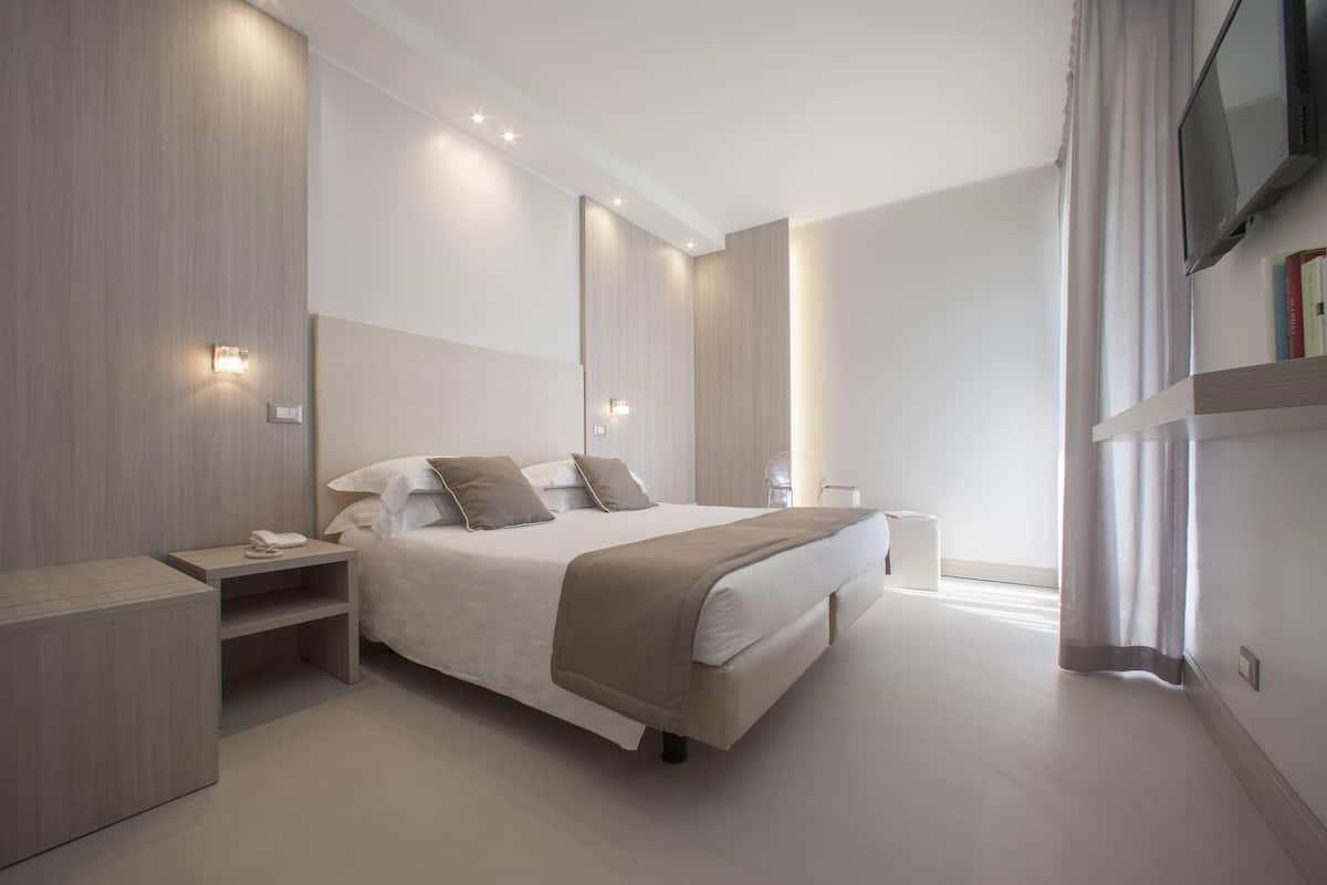 A modern hotel room with a large bed, bedside tables, a TV, and a bookshelf.