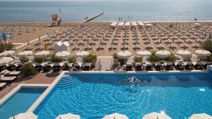 A poolside view with a beach in the background, sun loungers, umbrellas, and a lifeguard tower. - Hotel delle Nazioni (Jesolo)