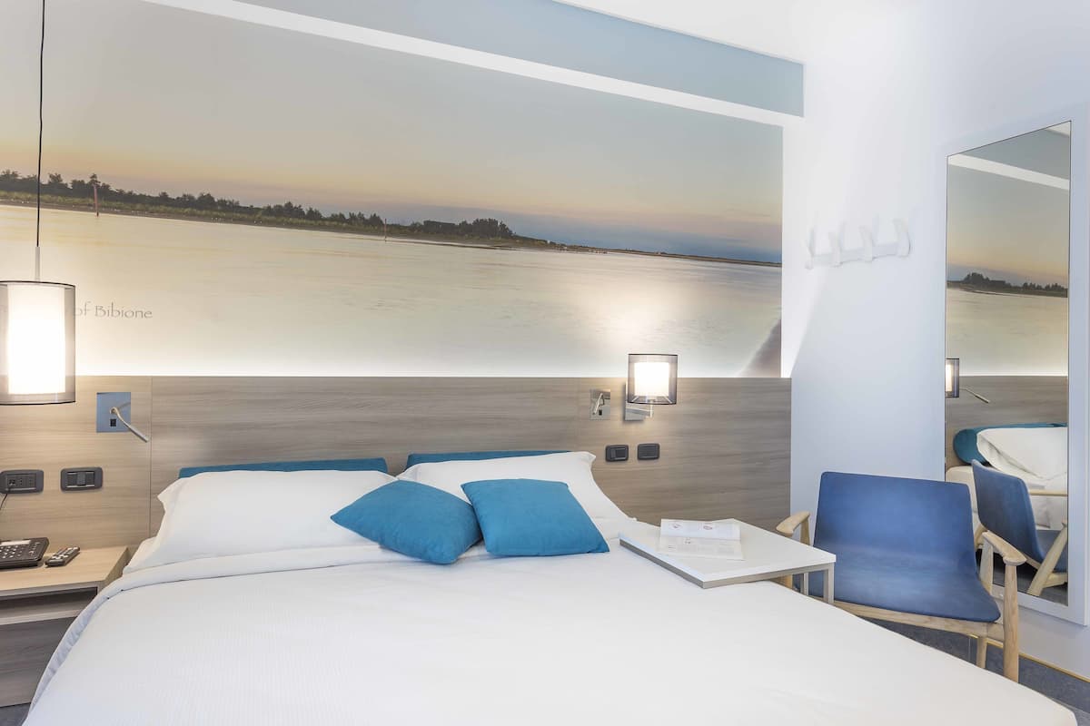 A hotel room with a bed, a desk, a chair, and a large window with a view of a body of water.