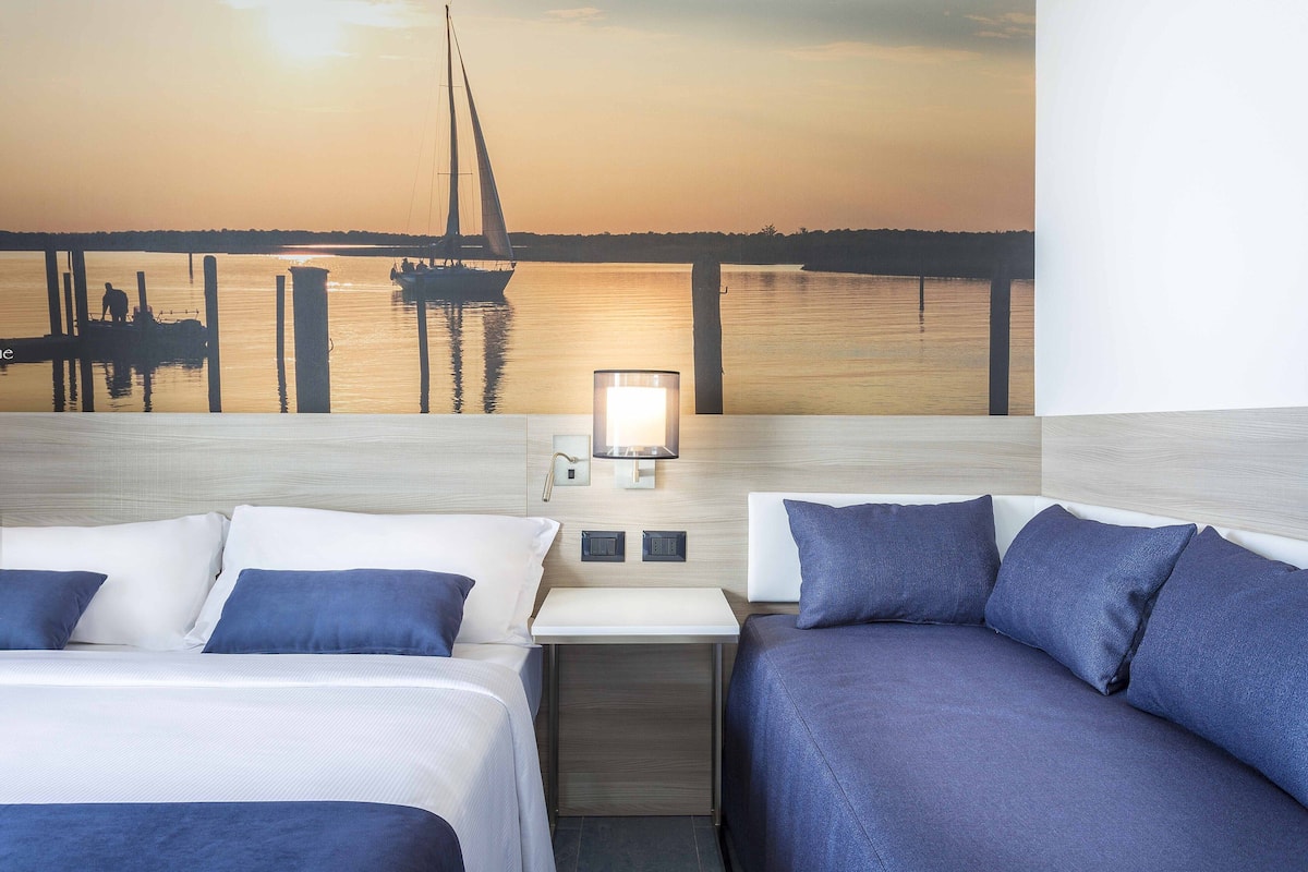 A hotel room with two beds, a nightstand, and a wall-mounted lamp.
