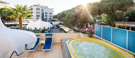 A rooftop pool area with a hot tub, lounge chairs, and umbrellas.
