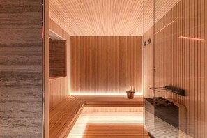 A modern sauna room with wooden walls, a glass partition, and a built-in fireplace.