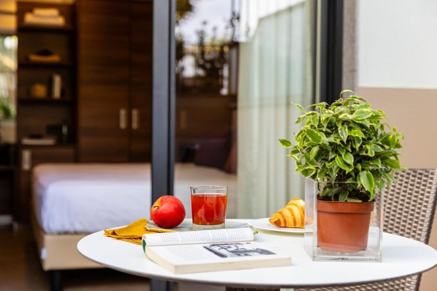 A table with a book, a glass of juice, a fruit, and a croissant.
