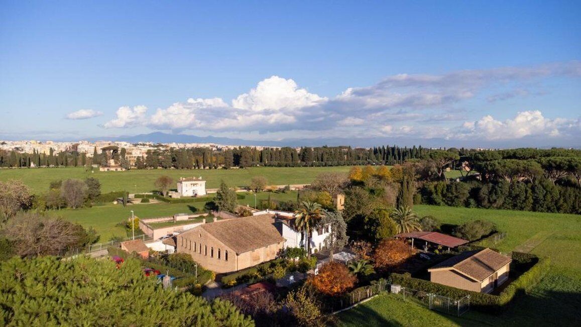 A large building with a flat roof, surrounded by green fields and trees.