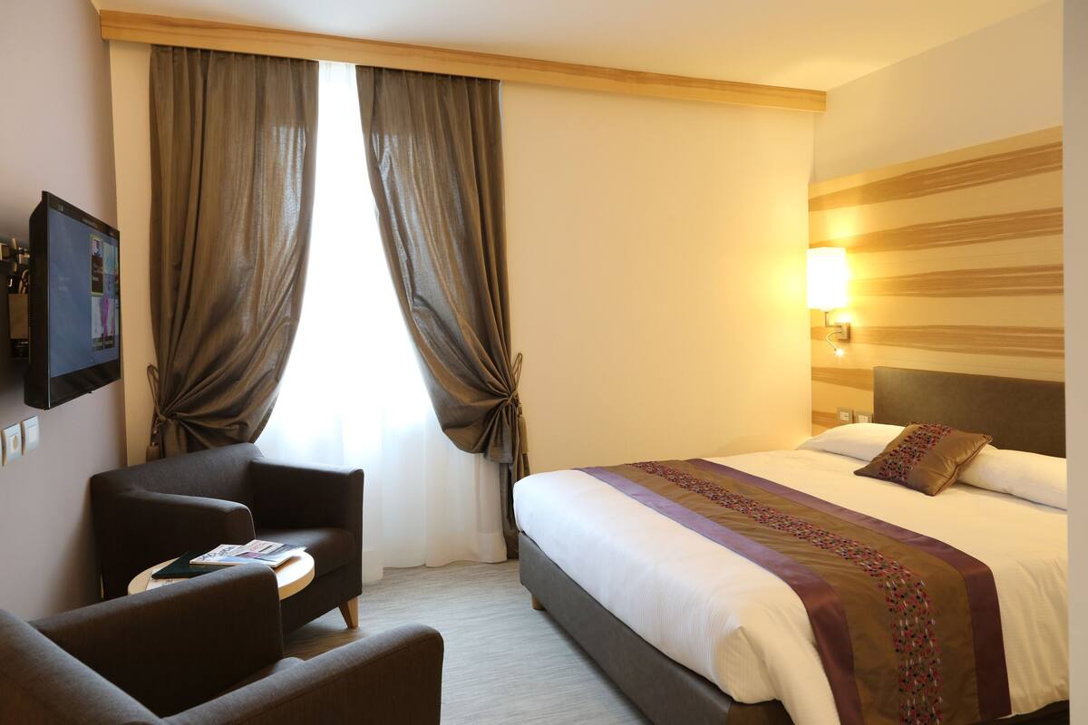 A hotel room with a bed, a sofa, a TV, and a lamp.