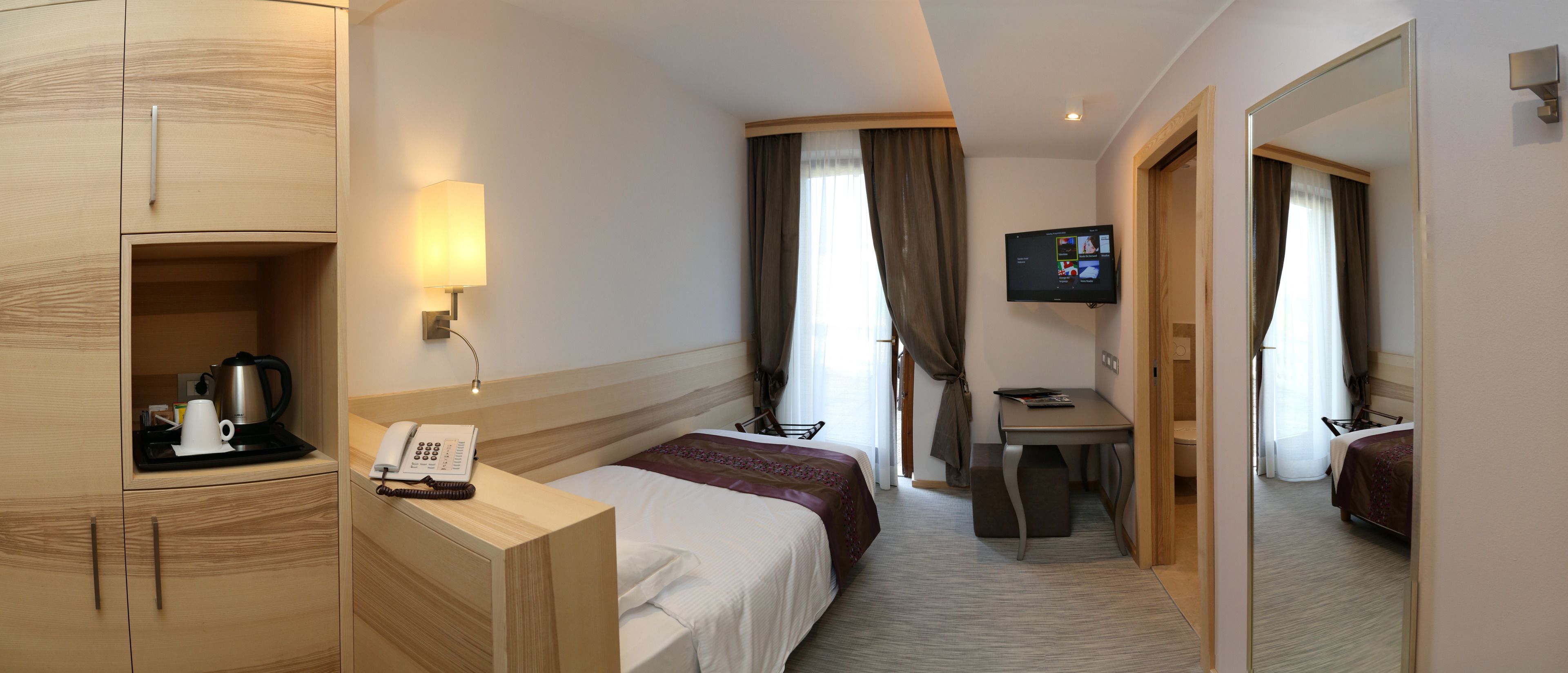 Una habitación de hotel con cama, mesita de noche, lámpara, televisión y escritorio.