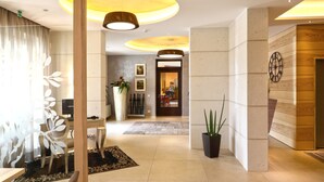 Een moderne hotellobby met een centraal receptiebalie, planten in potten en een grote klok aan de muur.
