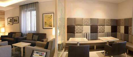 Una habitación de hotel moderna con un conjunto de sofás, una mesa de comedor y un cabecero estampado.