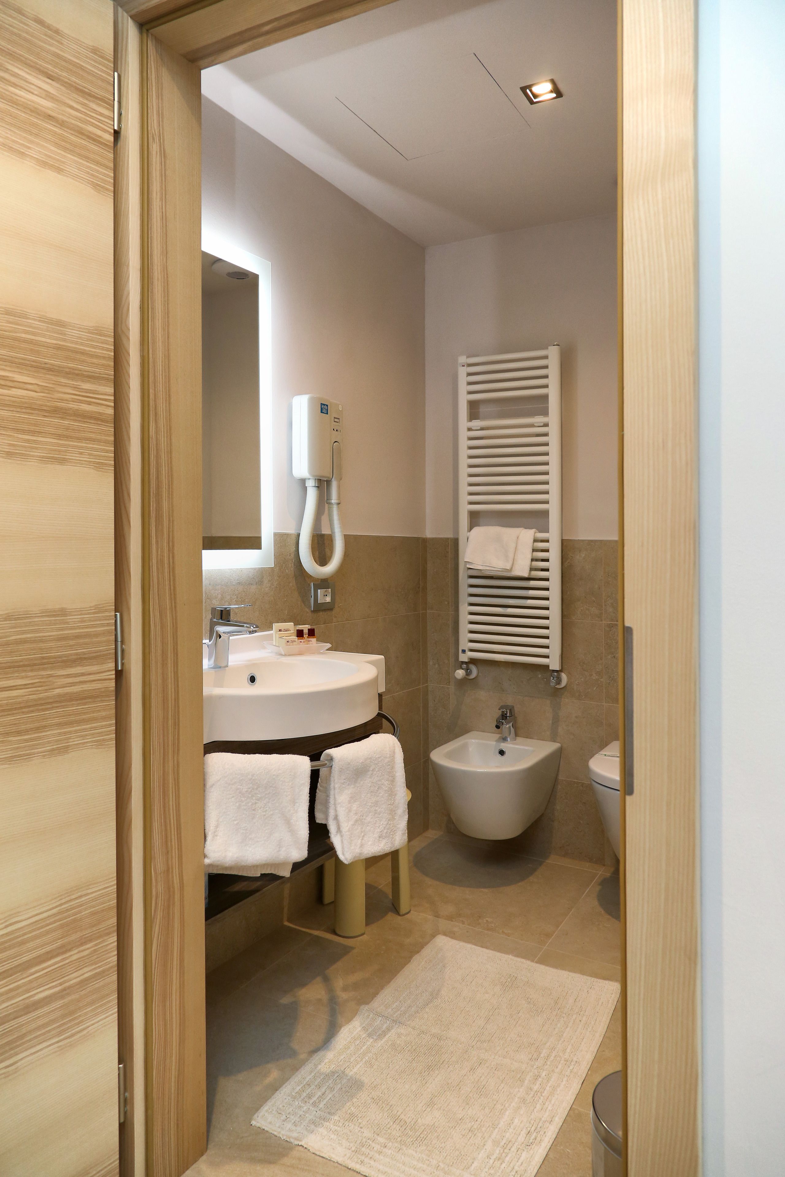 A modern bathroom with a wooden door, a sink with a mirror, a bidet, and a towel rack.