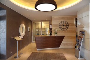 Una moderna zona de recepción con un mostrador de madera, un reloj grande y un atril para revistas.