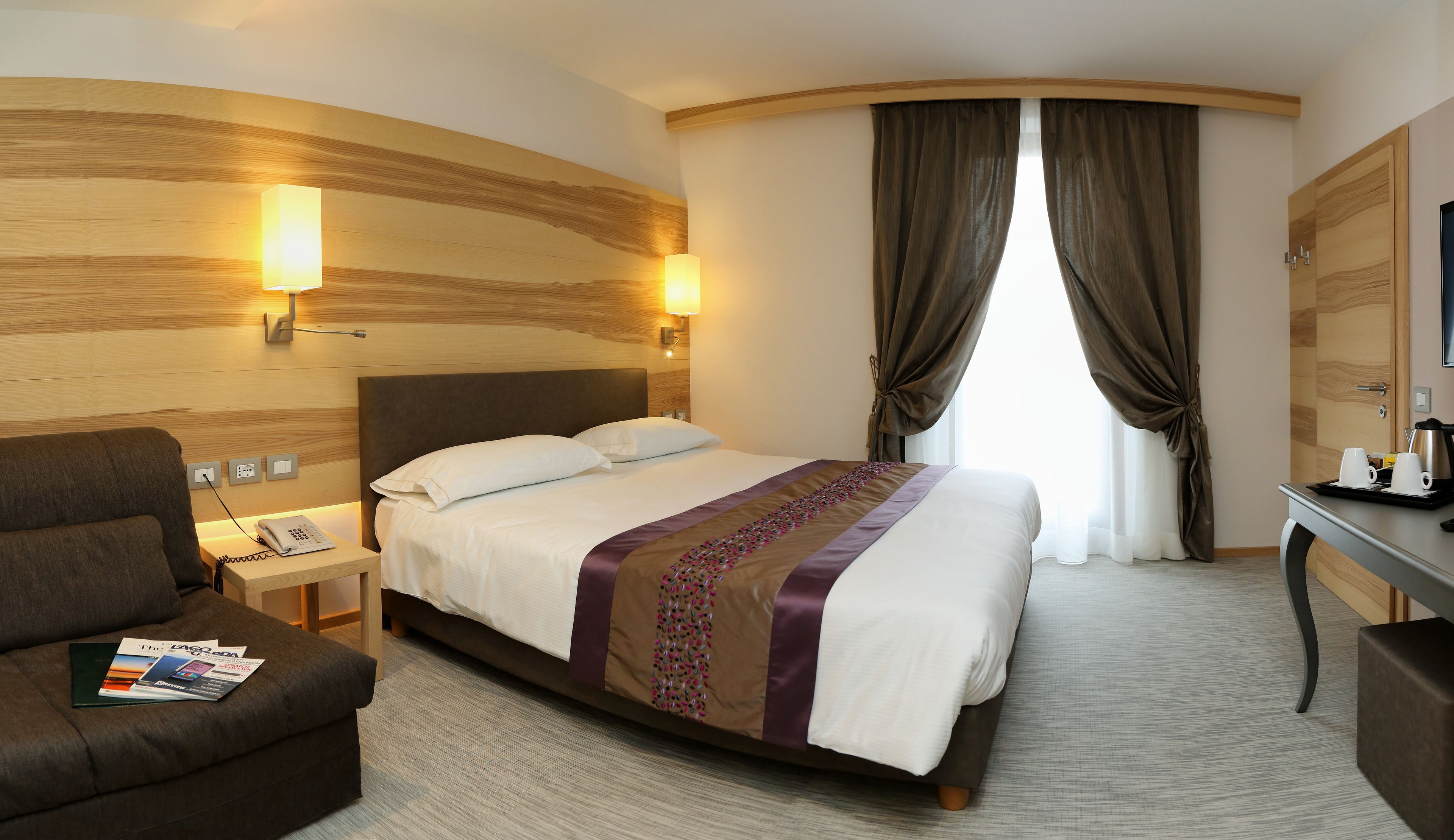 A hotel room with a large bed, a desk with a chair, a sofa, and a TV.