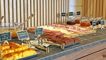 Ein reichhaltiges Buffet mit verschiedenen Speisen, darunter Torta, Makkaroni und unterschiedliche Käsesorten.