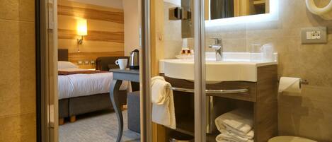 A hotel room with a bed, bedside table, lamp, and a bathroom with a sink, mirror, and toilet.