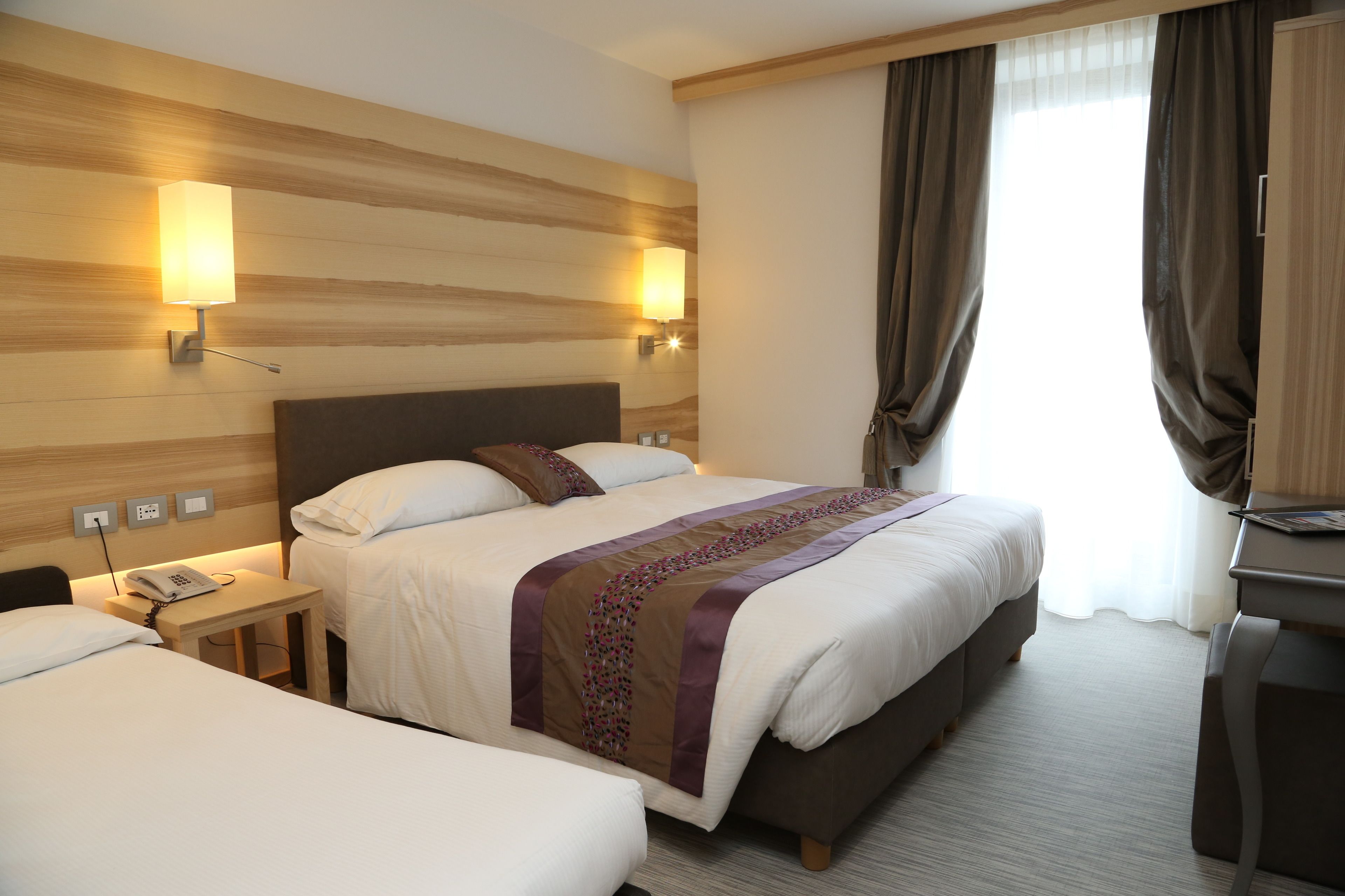 A hotel room with two beds, a desk, a phone on the nightstand, and a lamp on the wall.