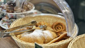A basket of pastries and bread, including croissants and a cinnamon roll, with tongs resting on top. - Hotel Garden (Peschiera del Garda)