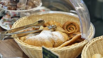 Una cesta con bollería y pan, incluyendo croissants y un rollo de canela, con unas pinzas encima.