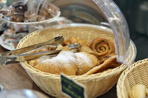 Una cesta con bollería y pan, incluyendo croissants y un rollo de canela, con unas pinzas encima.