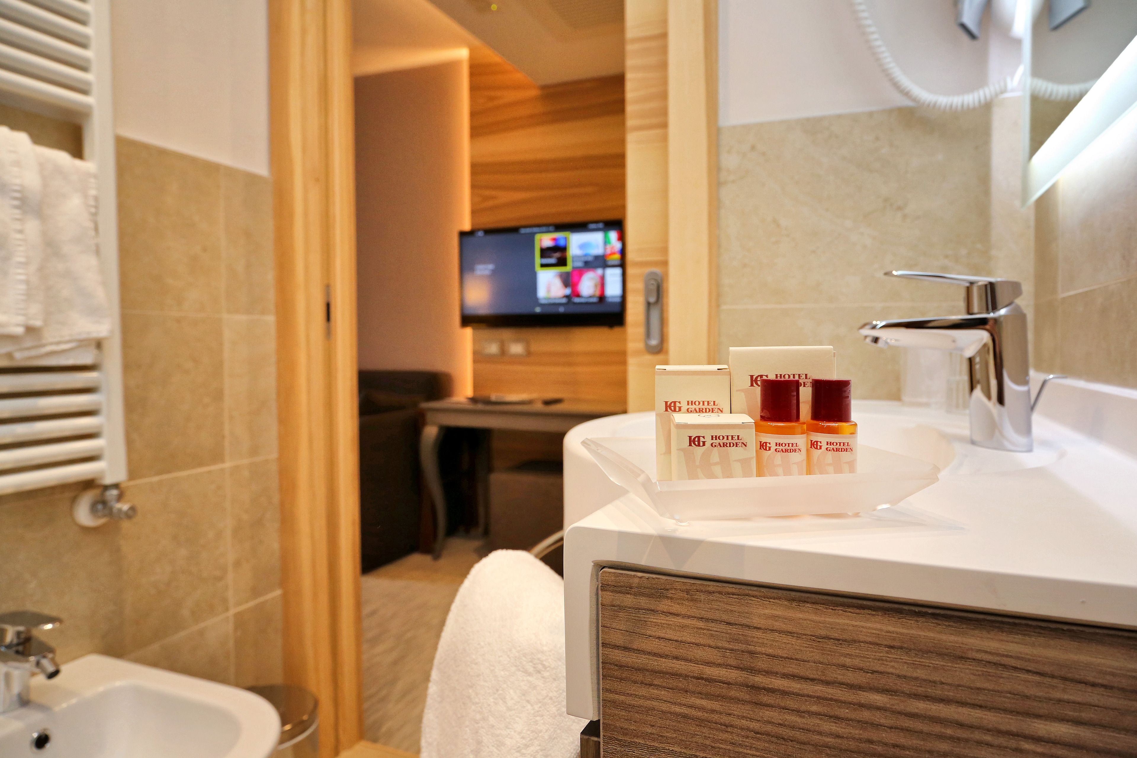 Un bagno d'albergo con lavandino, specchio e articoli da toilette. In secondo piano, un televisore è montato a parete.