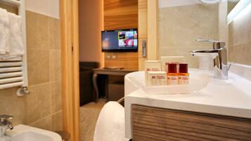 Un bagno d'albergo con lavandino, specchio e articoli da toilette. In secondo piano, un televisore è montato a parete.
