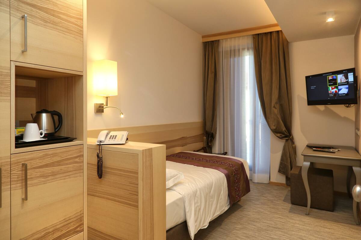 A hotel room with a bed, a desk, a TV, a telephone, and a coffee maker.