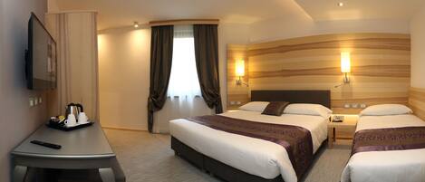 A hotel room with a large bed, a desk with a remote control, a coffee maker, and a TV on the wall.