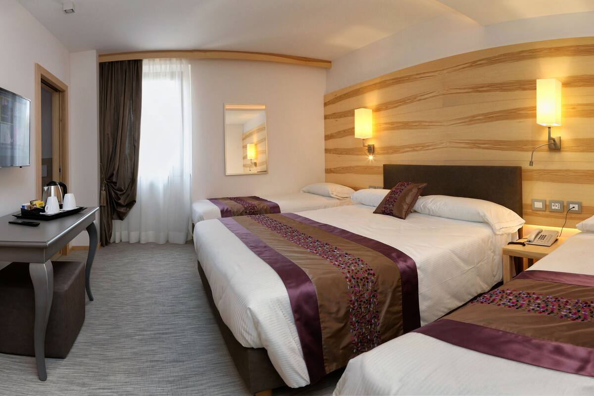 A hotel room with two beds, a desk, a TV, and a mirror.