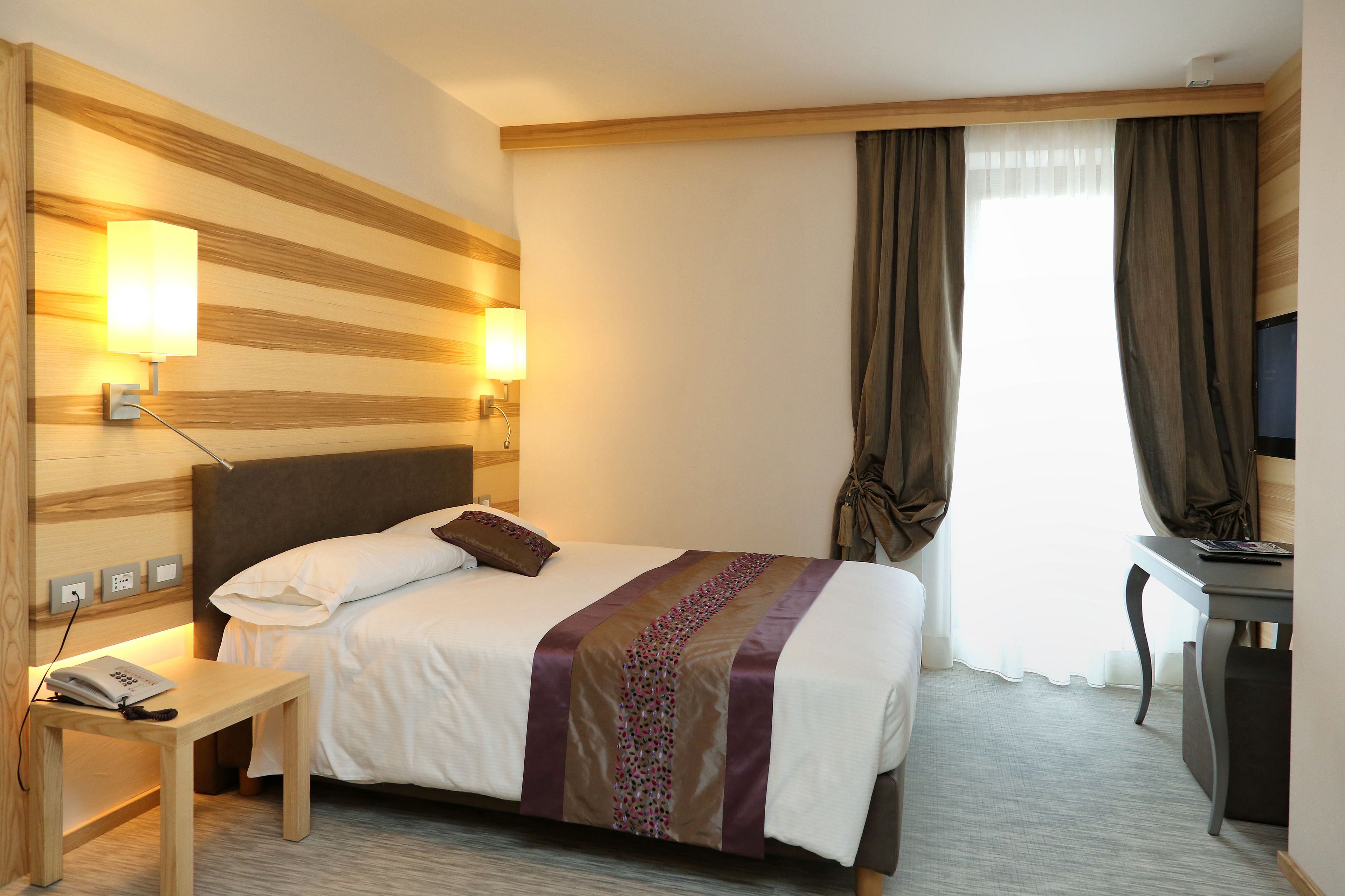 Une chambre d’hôtel comprenant un lit, une table de chevet, une lampe et un bureau avec une chaise.