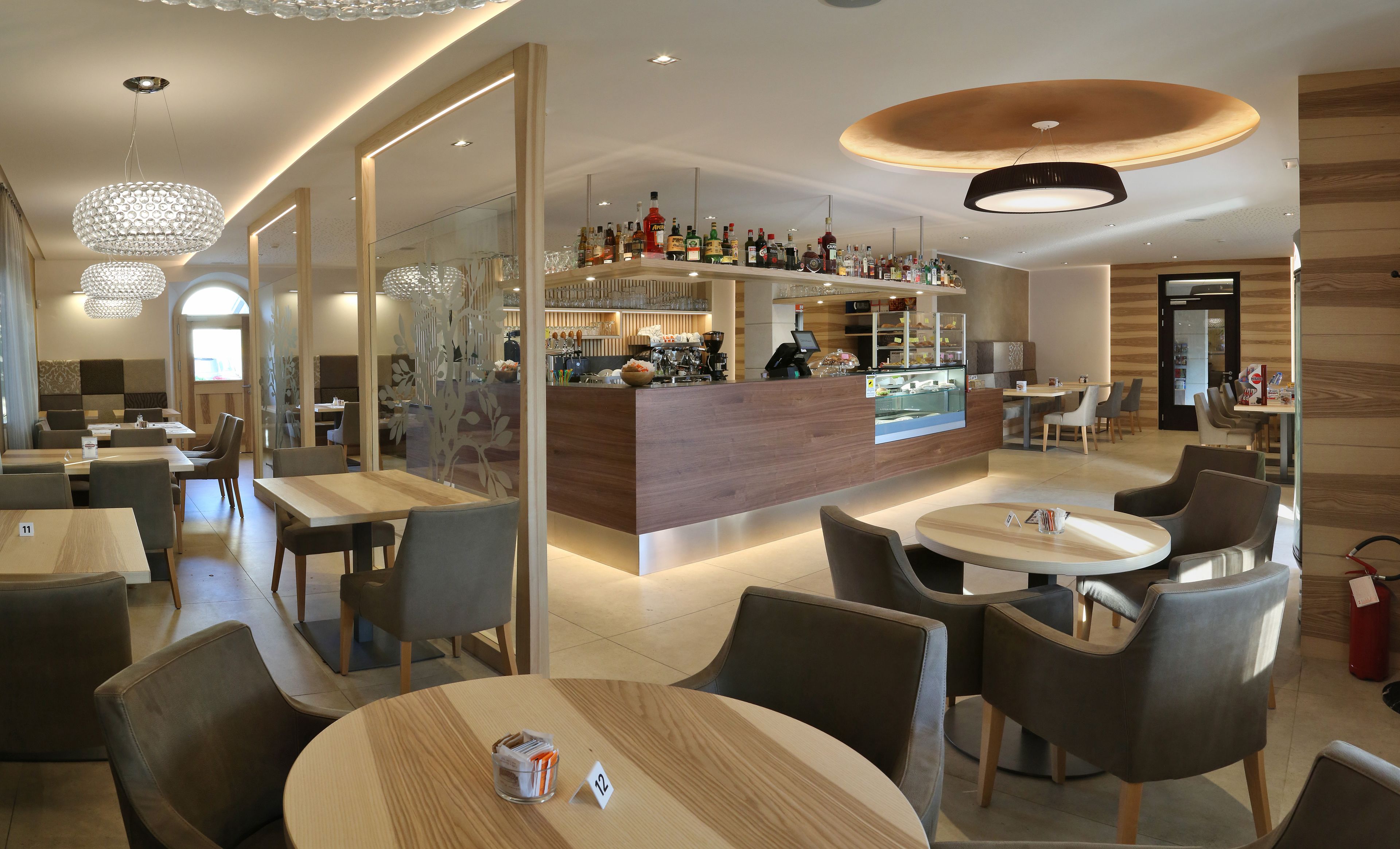 Un restaurante moderno con una zona de bar, mesas y sillas de madera, e iluminación decorativa.