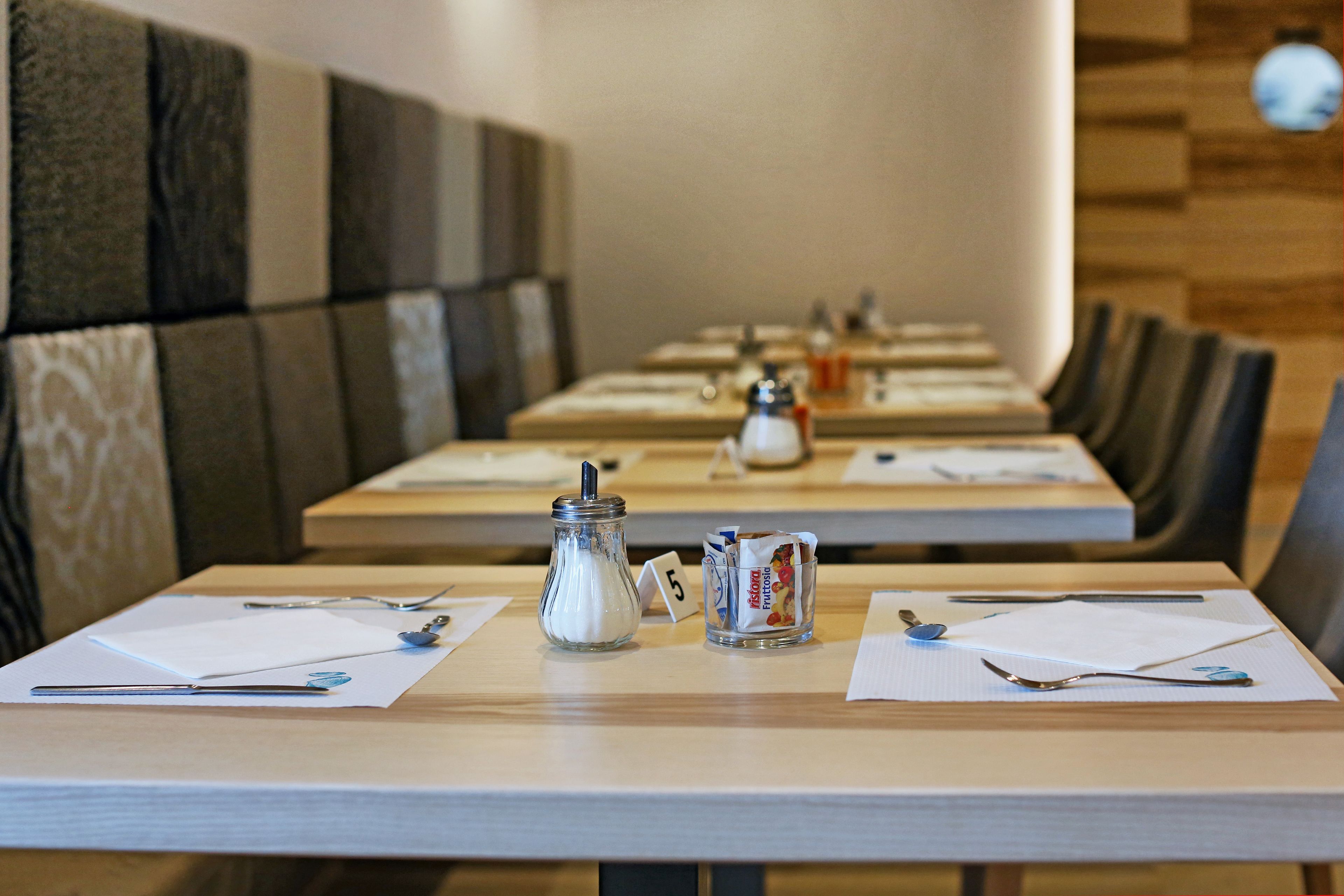 A restaurant with booths and tables, each with a menu, a salt and pepper shaker, and a small jar of condiments.