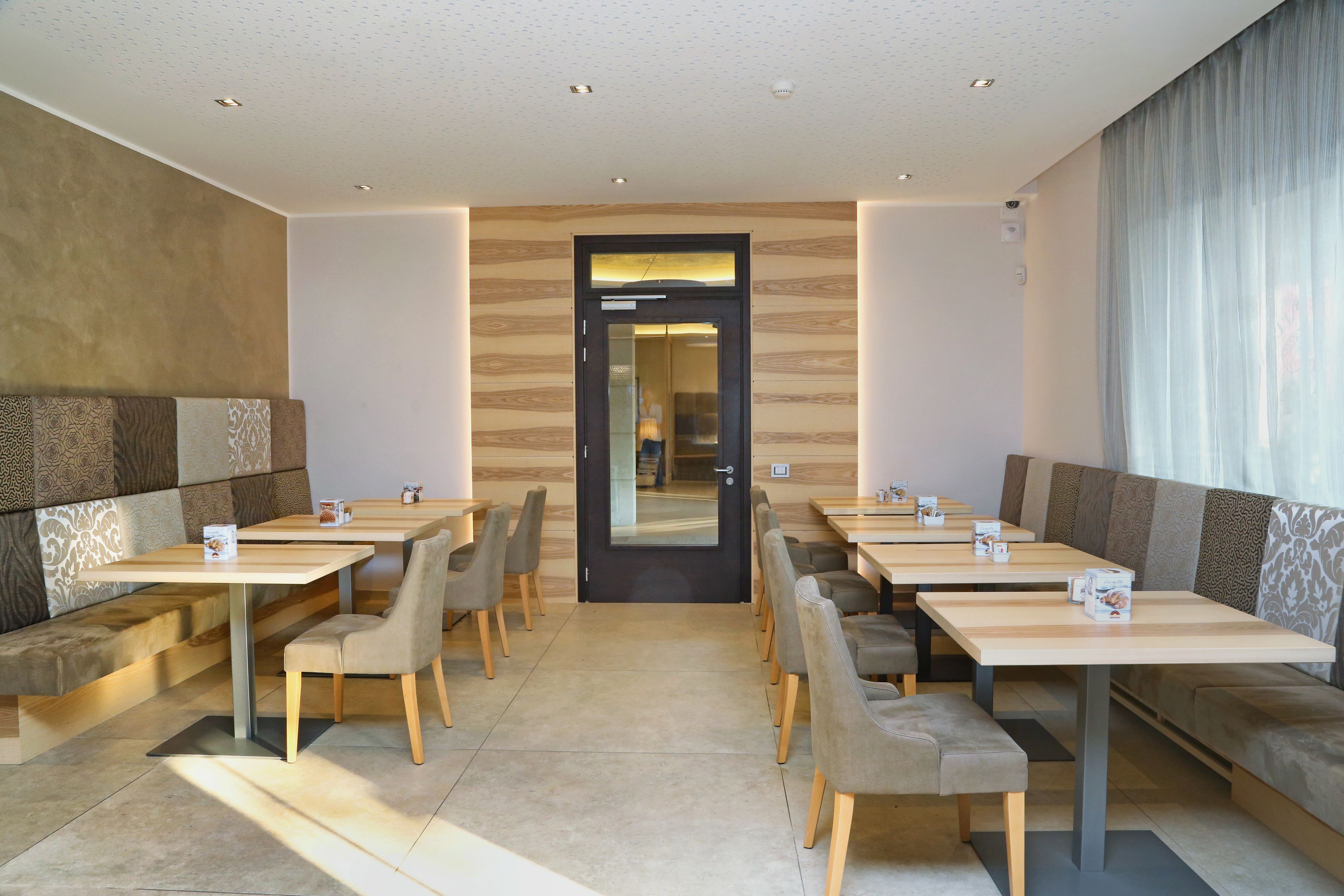 A modern hotel lobby with a central door, seating areas with tables and chairs, and a patterned wall.