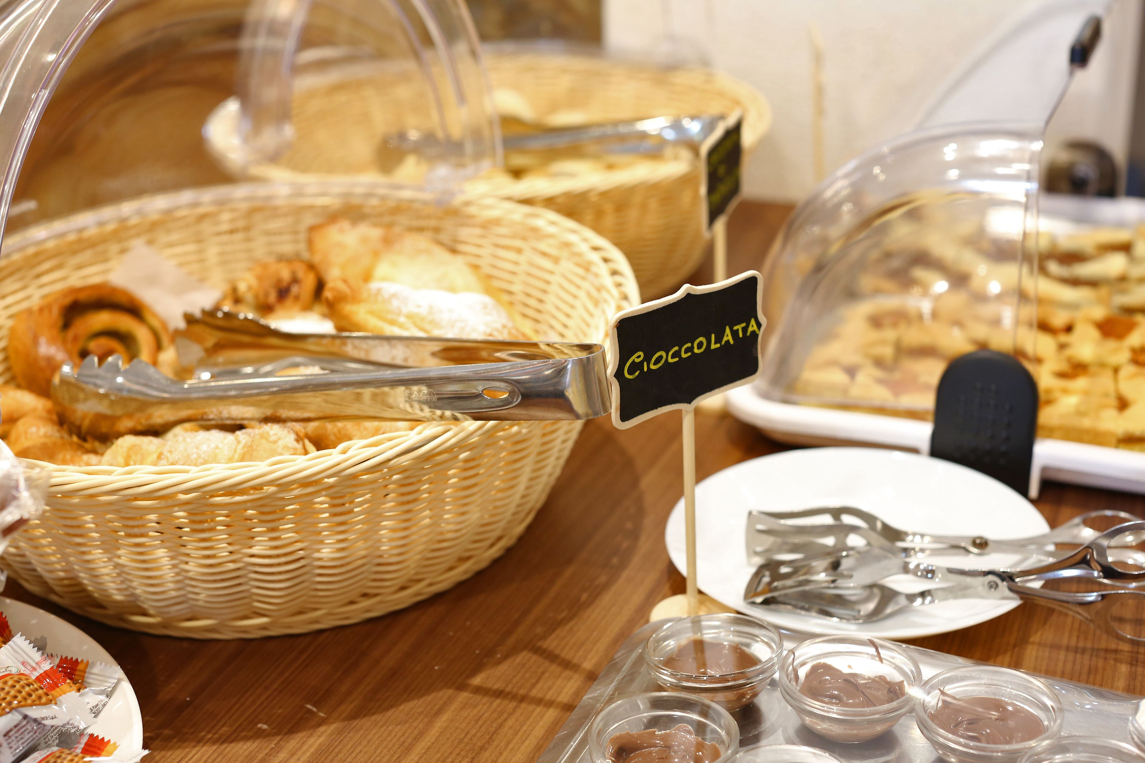 A buffet with various food items, including a basket labeled "Cioccolata" and a plate with tongs.