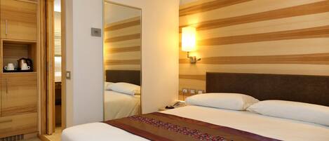 Une chambre d’hôtel avec un grand lit, une armoire en bois, un miroir et une lampe fixée au mur.