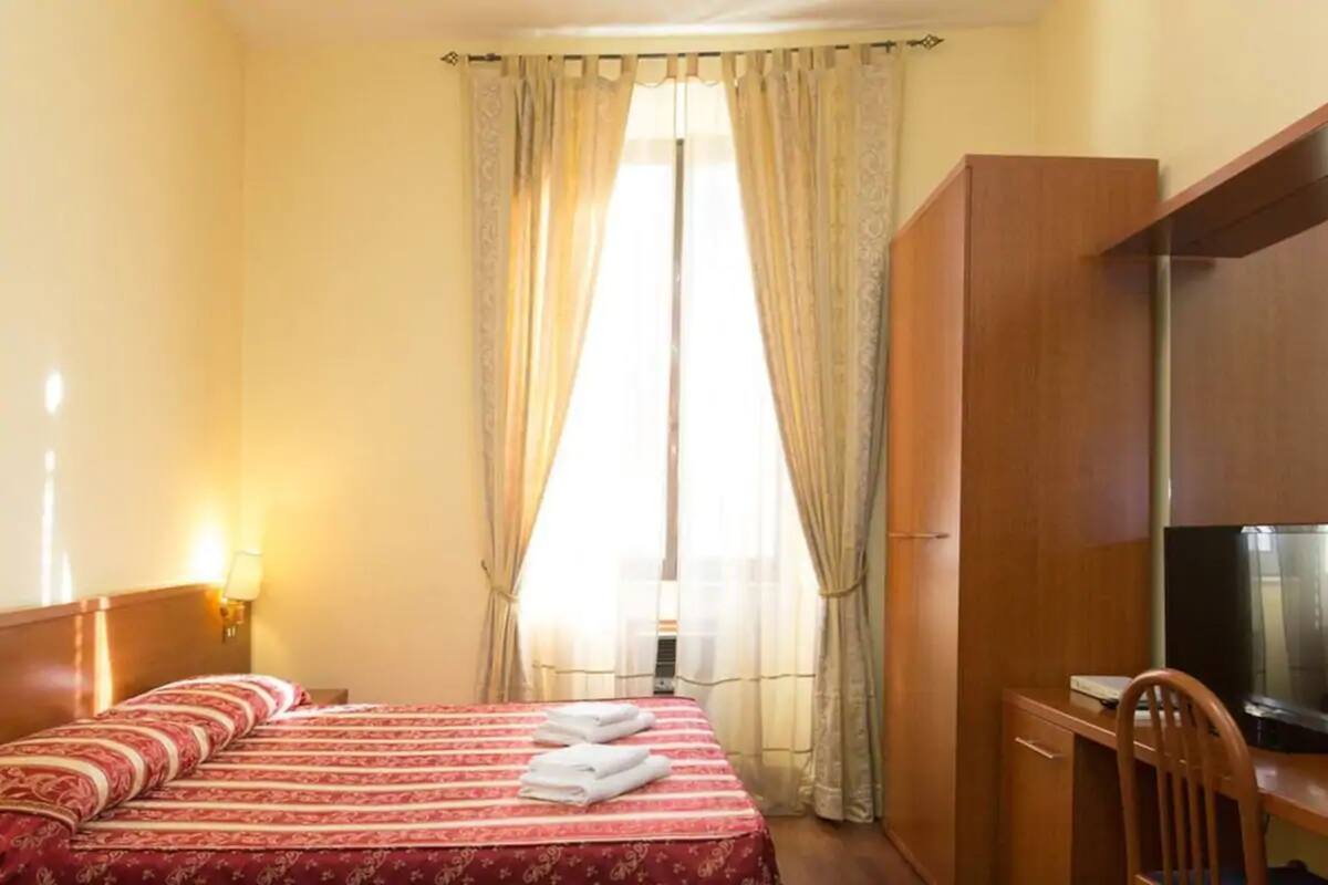 A hotel room with a bed, a desk, a television, and curtains.