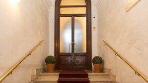 Une entrée imposante, avec une grande porte en arc de cercle, un tapis rouge et deux plantes en pot de chaque côté.