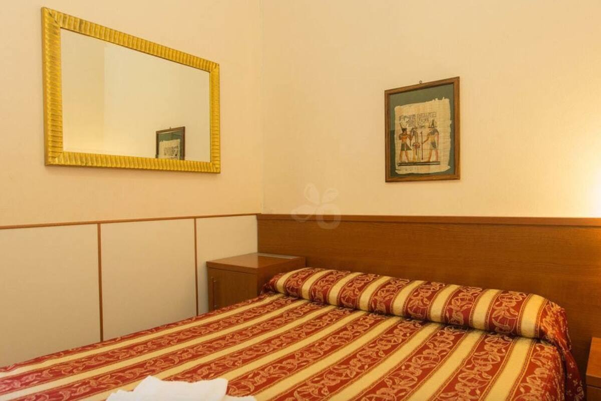 A hotel room with a bed, a nightstand, a mirror, and a framed picture on the wall.