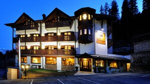 A multi-story hotel with balconies, a sign indicating it is a hotel, and a parking area in front. - Hotel Montana (Pinzolo)