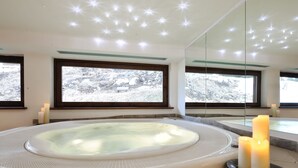 A modern bathroom with a large bathtub, candles, and a view of a snowy landscape through large windows. - Hotel Montana (Pinzolo)