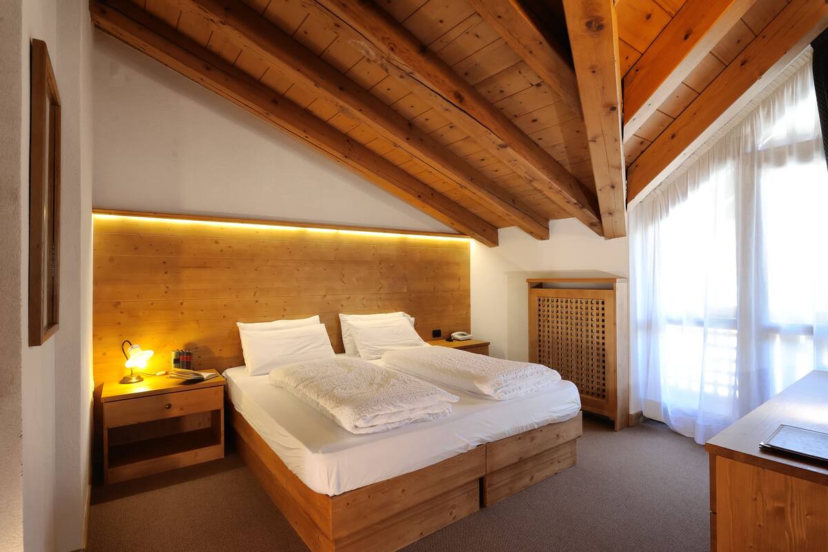A wooden bedroom with a bed, nightstands, and a desk.