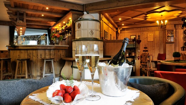 A wooden interior with a bar area, a table with a bottle of champagne, and a bowl of strawberries. - Hotel Montana (Pinzolo)